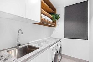 Une cuisine moderne dotée d’un évier encastré, d’un plan de travail en marbre et d’un lave-linge intégré.