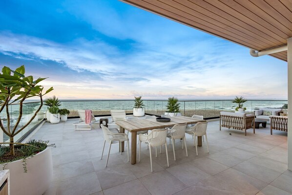Une terrasse avec une table et des chaises, des plantes en pot et une vue sur la mer.