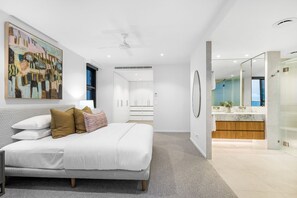 Une chambre moderne avec un grand lit, un ventilateur de plafond, une salle de bain avec une douche en verre et une vue sur la ville.