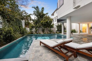 Une piscine entourée de chaises longues, de verdure et d’une architecture moderne.
