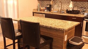 Eine Küche mit Granit Arbeitsplatte, dunklen Holzschränken, einem Edelstahlspülbecken und einem Mülleimer.