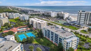 A coastal hotel complex with multiple buildings, a tennis court, and a parking area. - Luxury Beach Life: 3BR Condo w/ Ocean & Inlet View (New Smyrna Beach)
