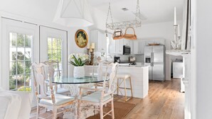 A bright kitchen with white cabinetry, a central island, and a dining area with white chairs. - The Brinley House:Steps from Beach/Pool/Bikes etc. (Destin)