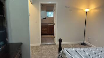 Une chambre à coucher comprenant un lit, une commode, une lampe et une porte donnant sur une salle de bain.