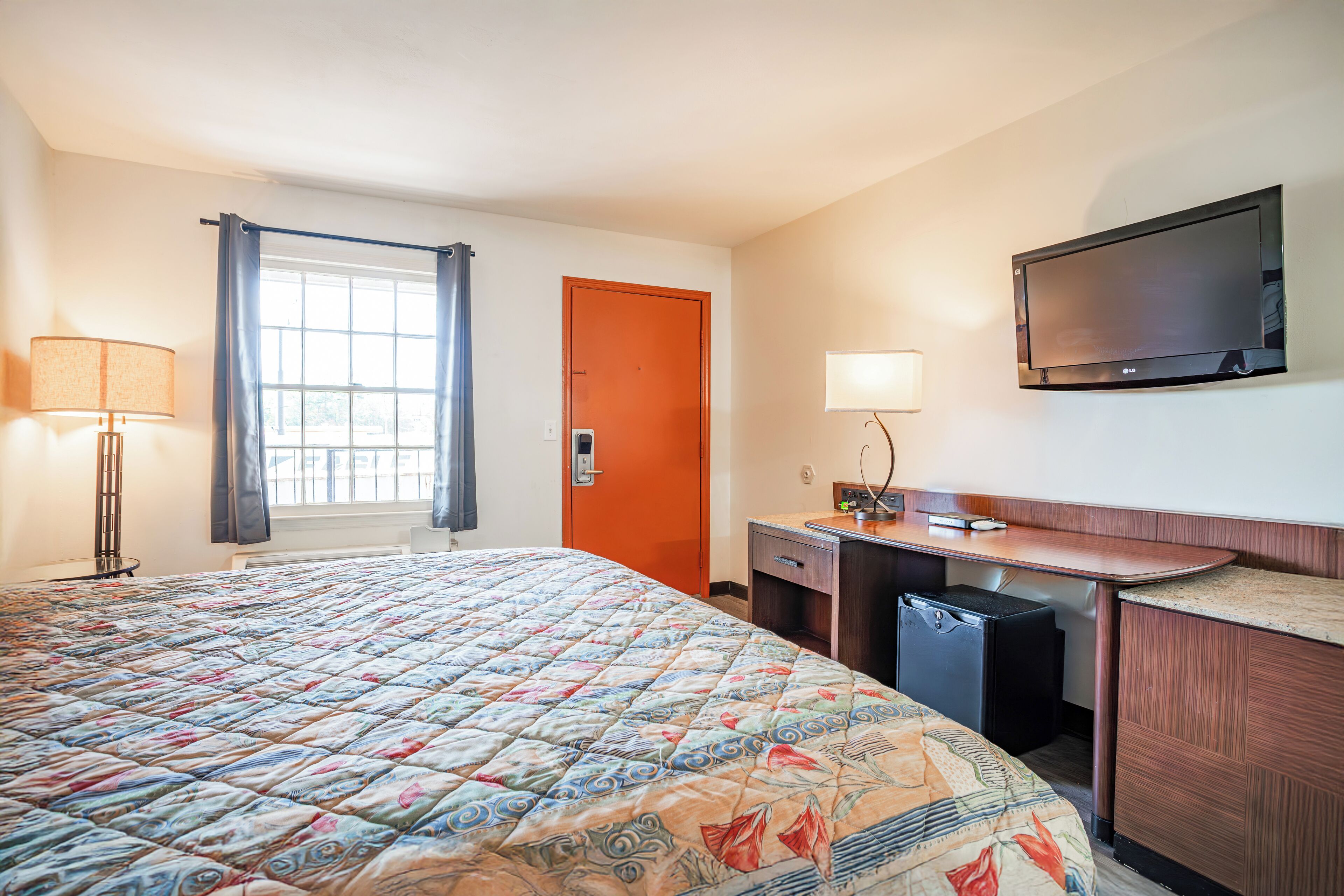 A hotel room with a large bed, a desk, a television, and a window with curtains.