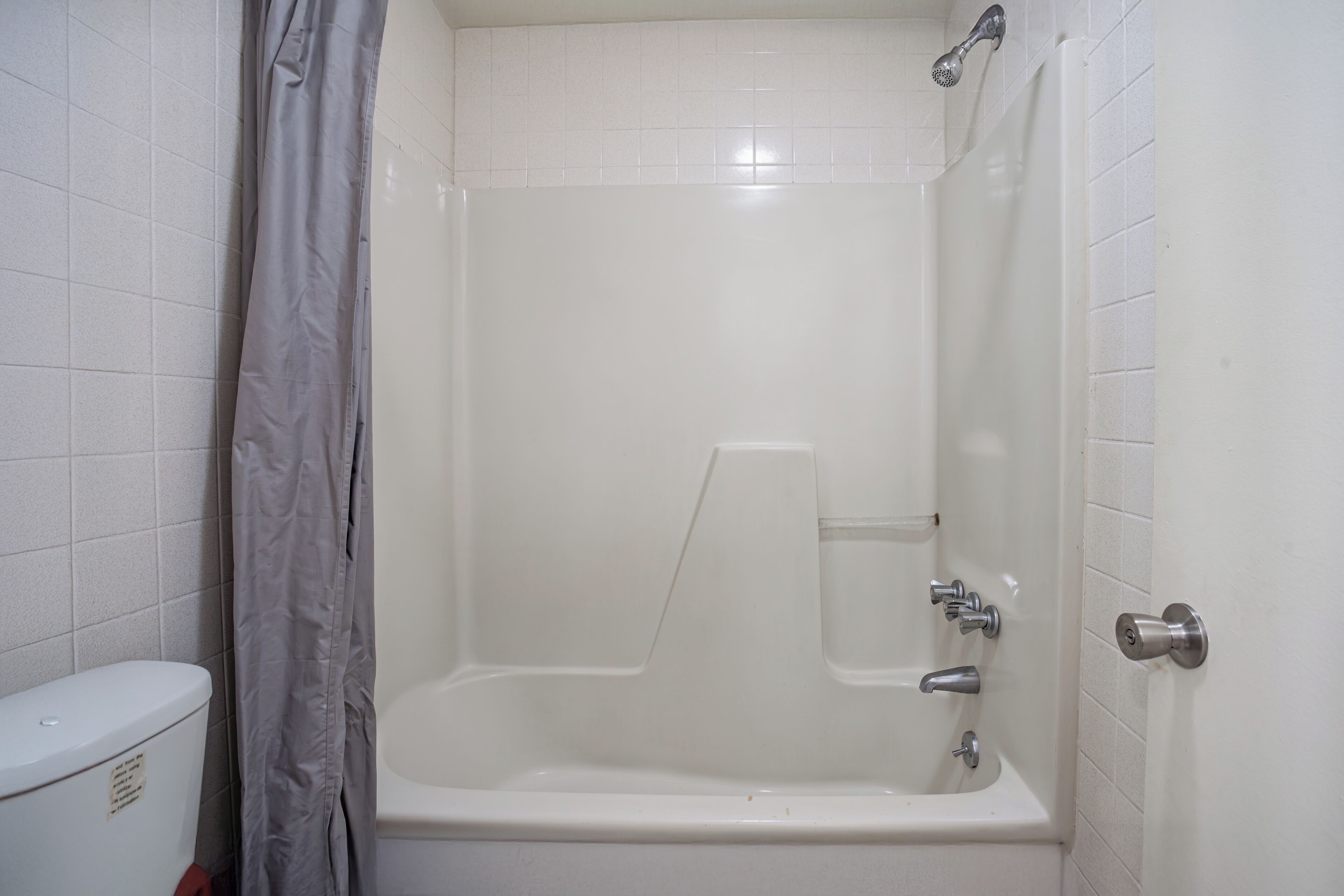 A bathroom with a white bathtub, a shower curtain, and a toilet.