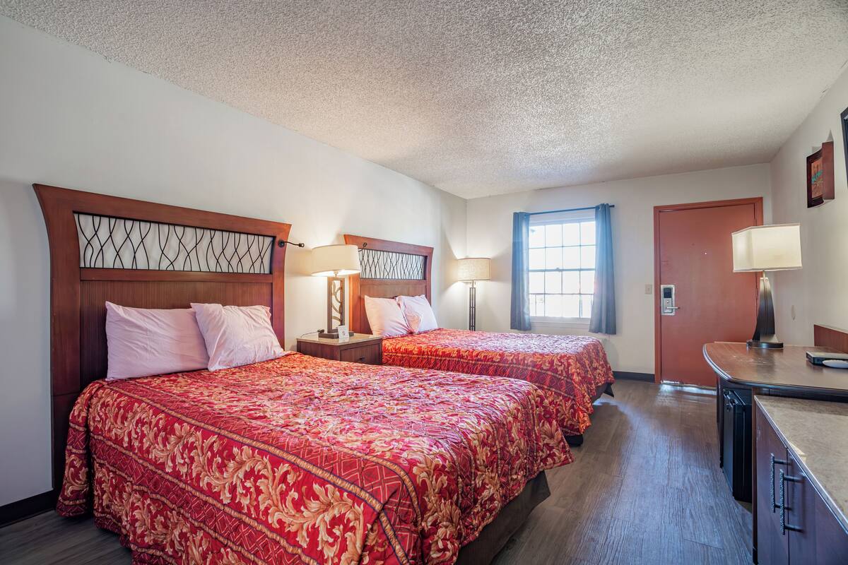 A hotel room with two beds, wooden headboards, and a desk with a lamp.