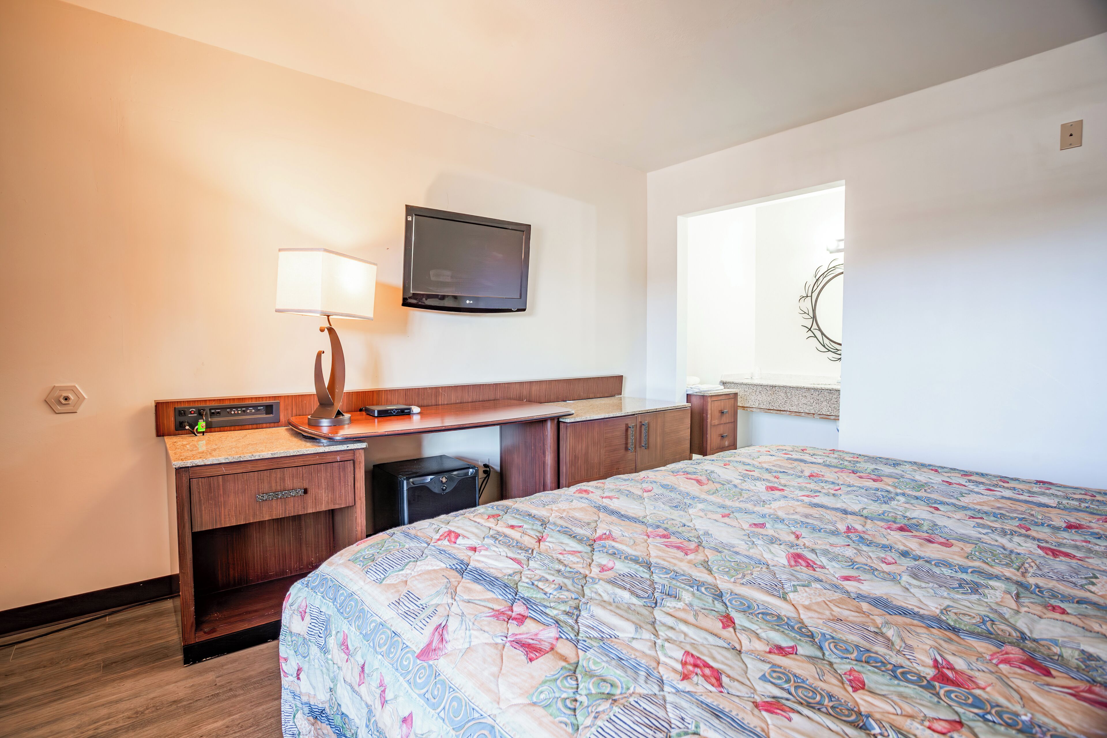 A hotel room with a bed, a desk with a lamp, a television, and a small refrigerator.