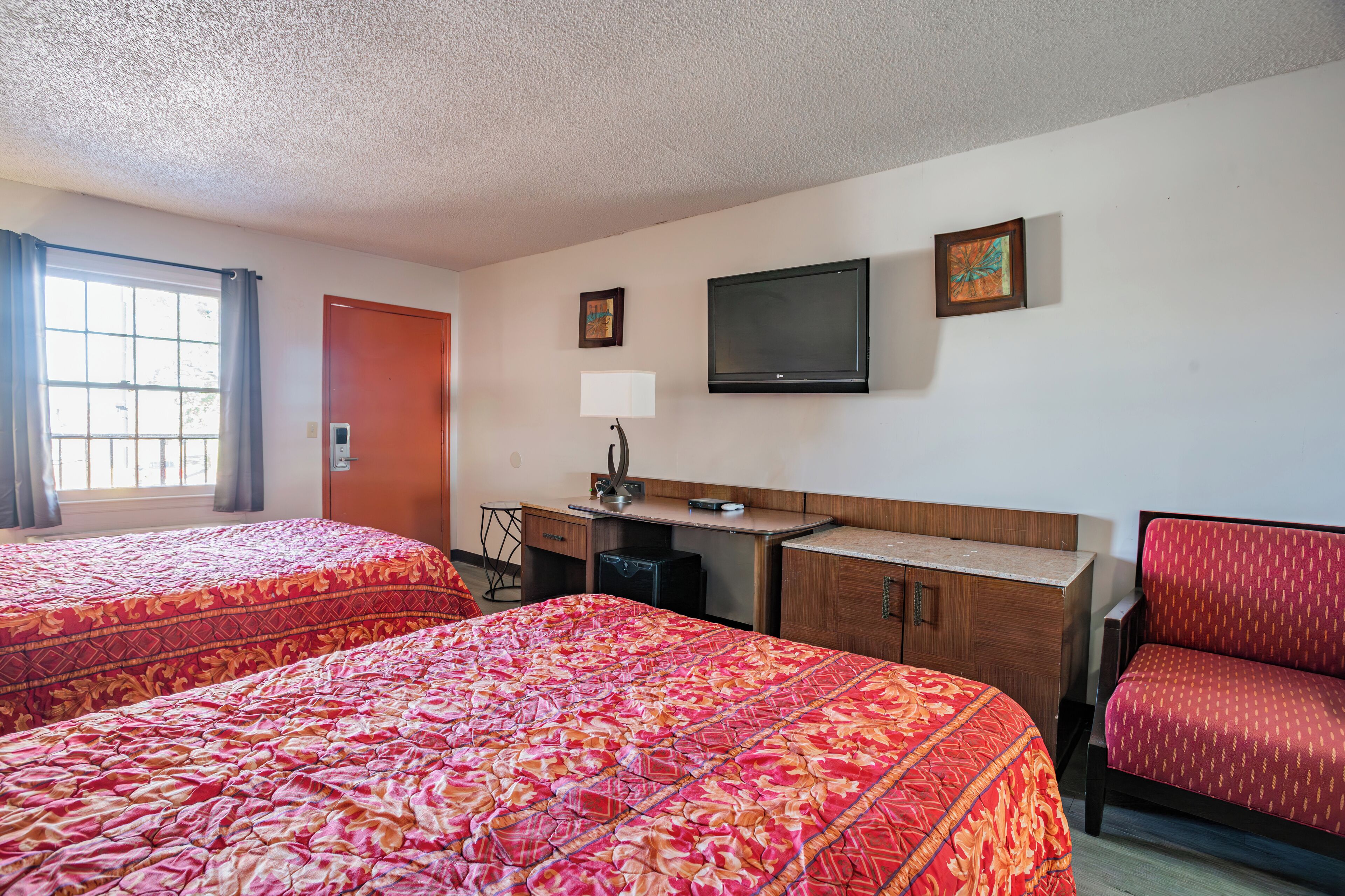 A hotel room with two beds, a desk, a chair, a TV, and a window with curtains.