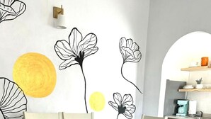 A dining area with a white table and benches, a yellow sun mural, and a kitchen in the background.