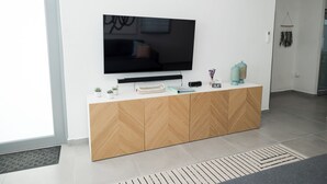 A modern living room with a large flat-screen TV mounted on a wooden cabinet, a small potted plant, and a decorative item on the cabinet.