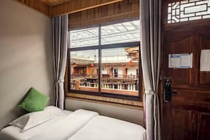 Una habitación con cama, ventana con vistas a arquitectura tradicional y puerta de madera.