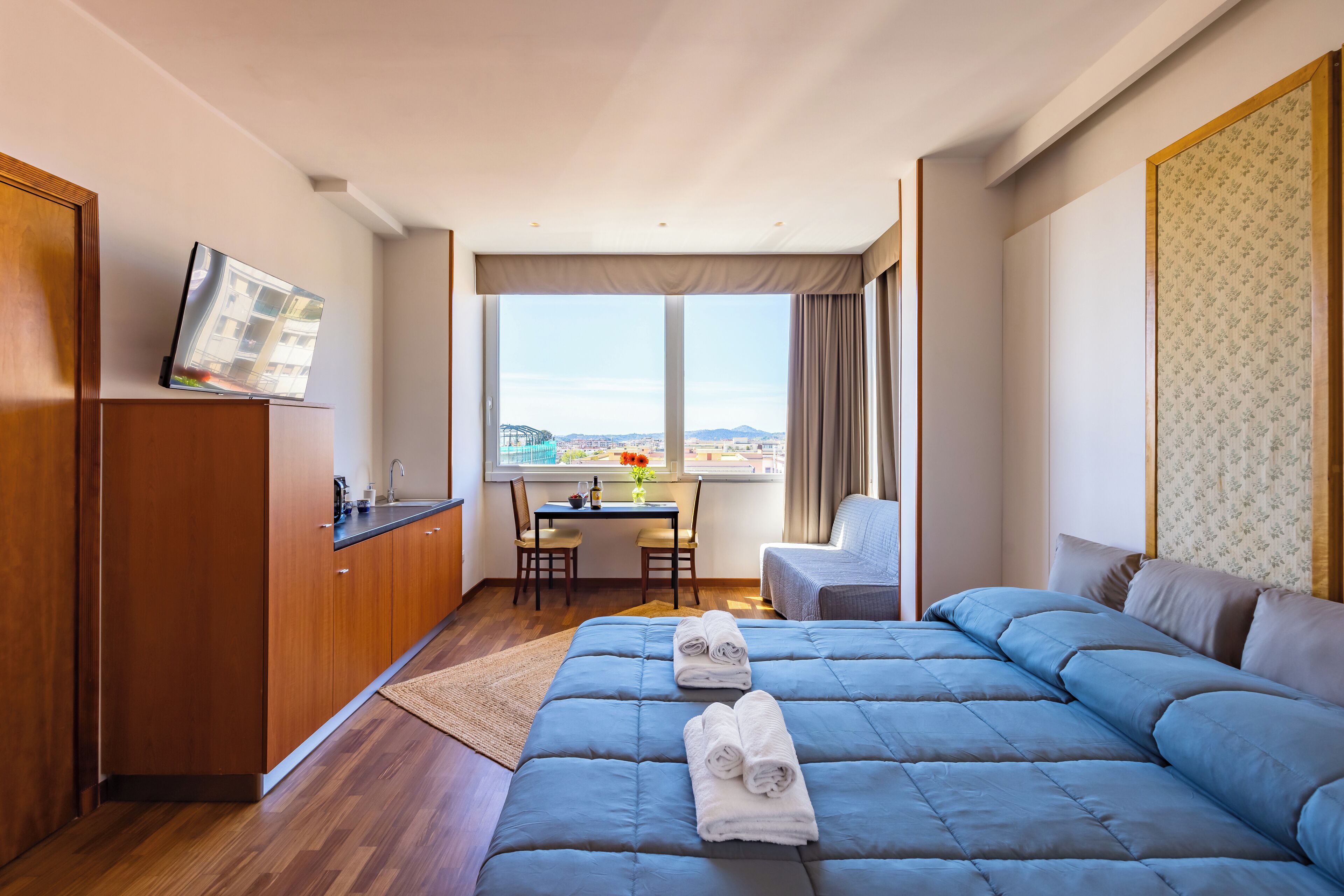 Une chambre d’hôtel avec un grand lit, un bureau avec deux chaises, un téléviseur fixé au mur et une vue sur la ville.
