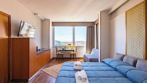 A hotel room with a large bed, a desk with two chairs, a TV on the wall, and a view of the city. - Chiave di Fuga - Tripla Superior - Camera 2 (Naples)