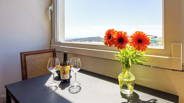 A table with a bottle of wine, two wine glasses, and a vase with flowers by a window. - Chiave di Fuga - Tripla Superior - Camera 2 (Naples)