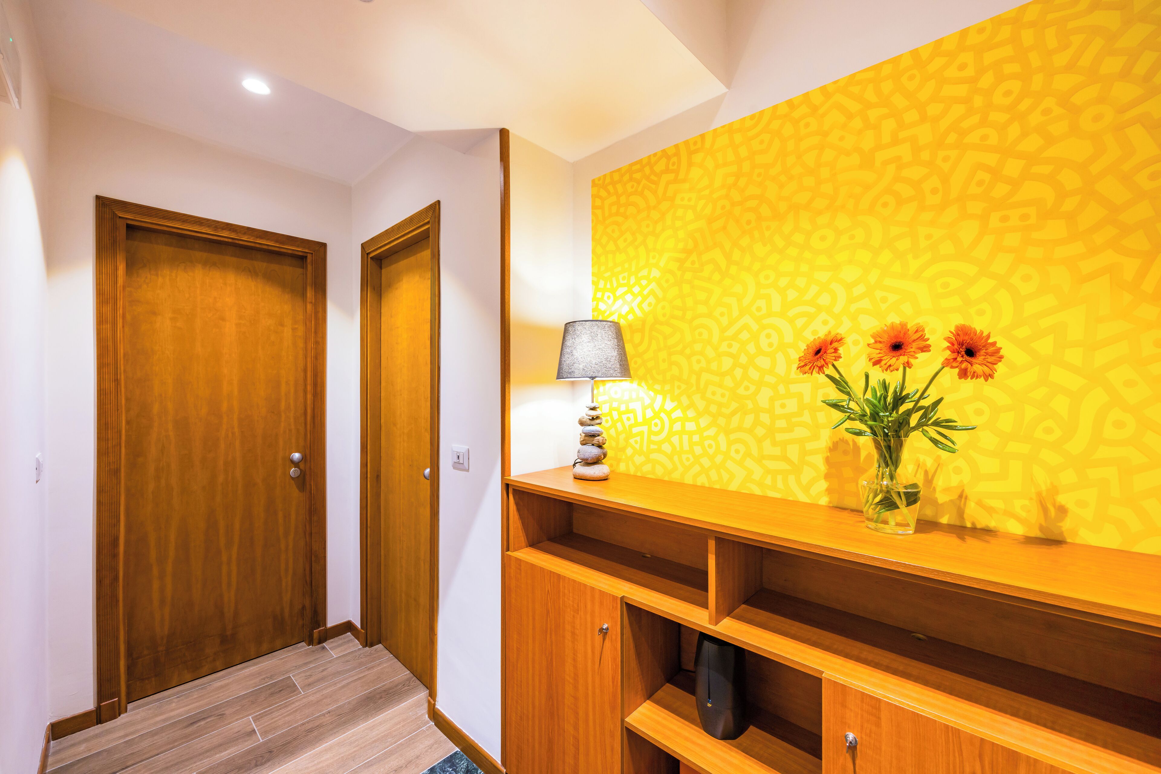 A hallway with wooden doors, a lamp, and a shelf with a vase of flowers.