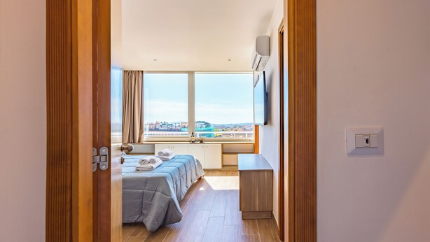 A modern hotel room with a large window, a bed, a desk, and a view of the cityscape. - Chiave di Fuga - Doppia Superior -  Camera 4 (Naples)