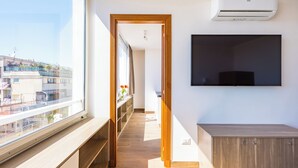 A modern apartment with a large window, a wooden bench, a flat-screen TV mounted on the wall, and a built-in air conditioning unit. - Chiave di Fuga - Doppia Superior -  Camera 4 (Naples)