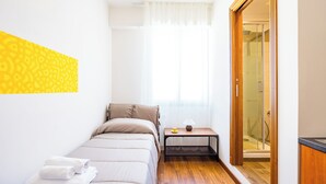 A small, well-lit bedroom with a bed, bedside table, and a shower area visible through a glass door. - Chiave di Fuga - Singola Classic - Camera 1 (Naples)