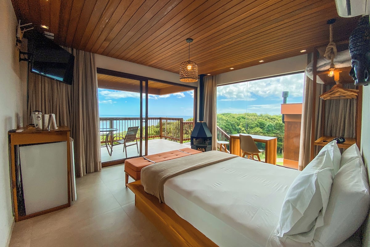 Une chambre d’hôtel avec un grand lit, un bureau, une chaise, une télévision et un balcon avec vue sur la mer.