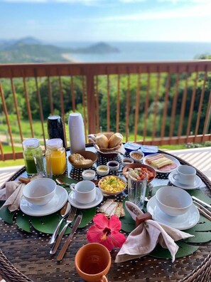 A breakfast setup on a balcony with a scenic view of mountains and greenery. - Reserva Pilger (Imbituba)
