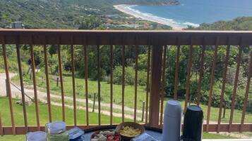 Una mesa de desayuno con diversas comidas y bebidas, con vistas a un paisaje costero con colinas y una playa.