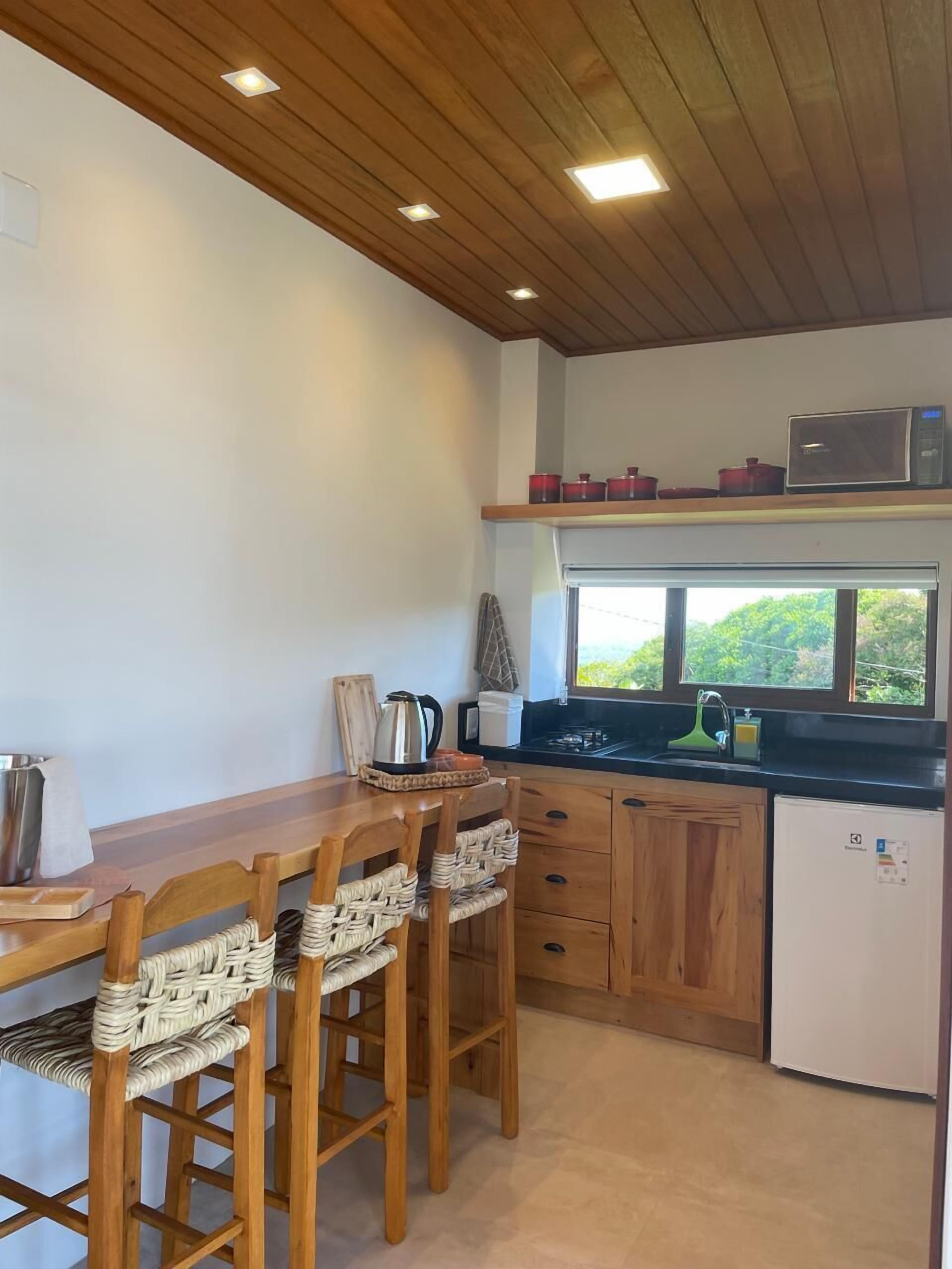 Uma cozinha compacta com armários de madeira, uma mesa de jantar com cadeiras, um micro-ondas e uma pequena geladeira.