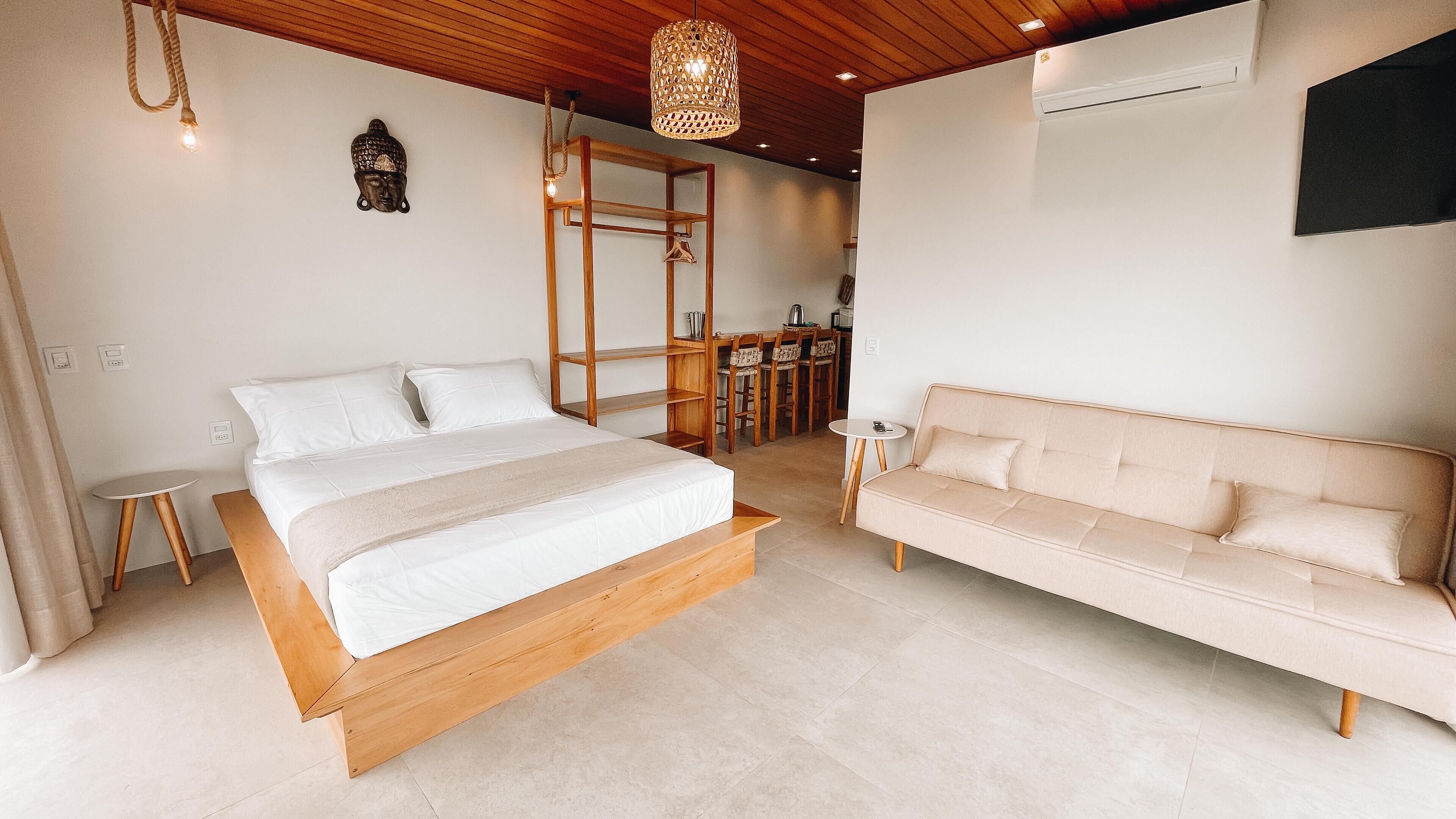 A bedroom with a wooden bed, a beige sofa, a wooden wardrobe, and a hanging light fixture.