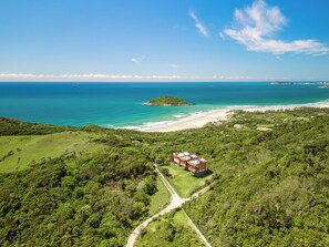 An aerial view of a coastal property with a beach, lush greenery, and a clear view of the ocean. - Reserva Pilger (Imbituba)