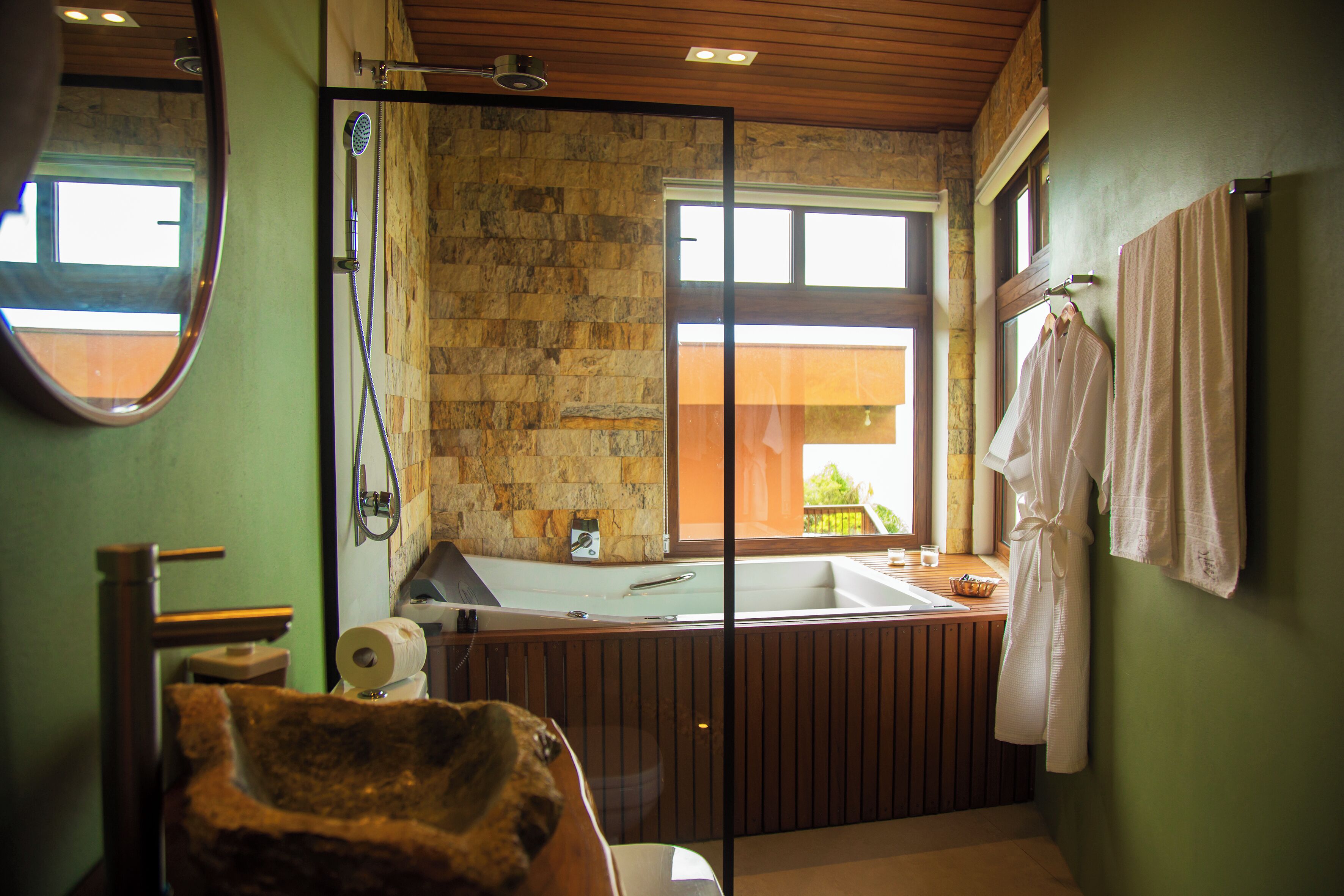 Ein Badezimmer mit Steinwand, großem Fenster, Badewanne und Spiegel.
