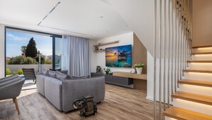 Un salon moderne avec un canapé gris, un plancher en bois et une grande fenêtre donnant sur un jardin.