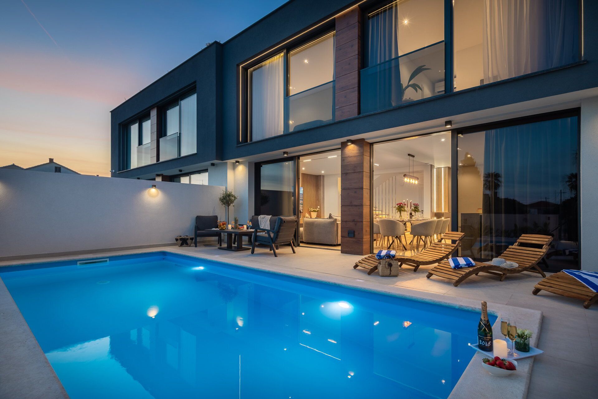 A modern house with a swimming pool, outdoor seating, and a dining area.