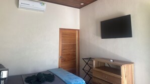 A bedroom with a ceiling fan, a TV mounted on the wall, a wooden wardrobe, and a bed with a blue blanket.