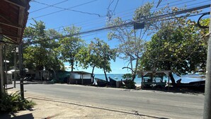 A coastal road with a clear view of the sea, a few boats, and a small building with a roof.