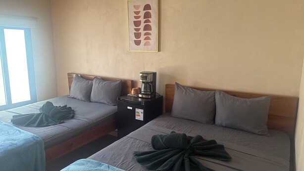 A hotel room with two beds, a coffee maker, a framed picture on the wall, and a window.