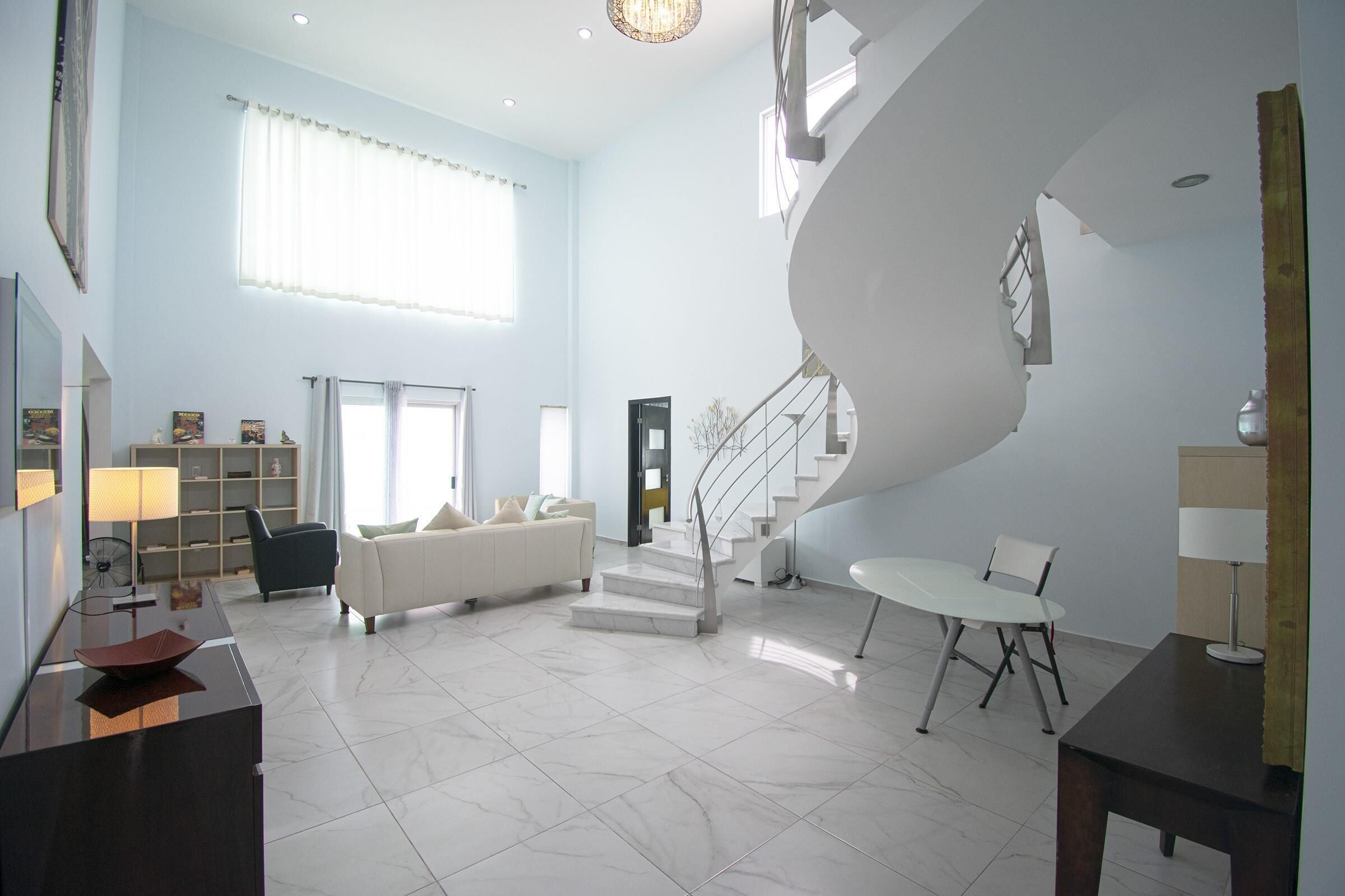 A spacious living area with a white sofa, a dining table, and a staircase leading to an upper level.