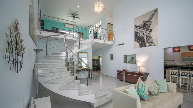 A spacious living area with a curved staircase, a sofa with cushions, a dining area, and a kitchen. - Entire home with Pool. Walk to the beach. Lety Copel (Mazatlan)