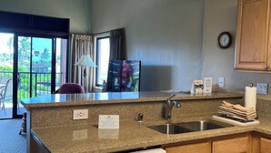 Una cocina con encimeras de granito, lavavajillas, armarios de madera, un fregadero y una ventana con cortinas.