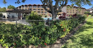Un hotel con varios balcones, piscina y un jardín bien cuidado con flores rojas.