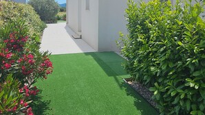 Un edificio moderno con fachada blanca, un sendero pavimentado y césped sintético verde.