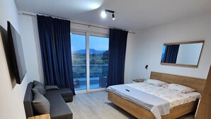 Un dormitorio moderno con una cama grande, un sofá, un banco de madera y un balcón con cortinas.
