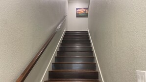 Eine Treppe mit dunklen Holzstufen und einem Holzgeländer, die zu einer Zwischenebene mit einem Gemälde führt.