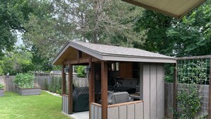 Eine kleine Holzhütte mit überdachter Terrasse, Grill und umzäunter Garten.