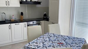 Et kompakt køkken med hvide skabe, en sort bordplade og et spisebord med dug med blomster.