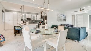 Et moderne køkken med hvide skabe, en central ø med siddepladser og et spiseområde med hvide stole.