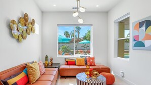 A modern living room with a sectional sofa, a round coffee table, and a large window with a view of outdoor umbrellas.