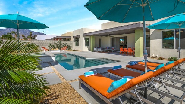 A modern outdoor pool area with lounge chairs and umbrellas, a pool, and a view of mountains.