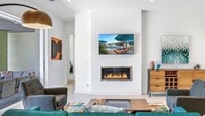 A modern living room with a fireplace, green sofas, a coffee table, and artwork on the walls.