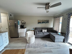 A modern kitchen with a refrigerator, coffee maker, and a dining area with a grey sofa and a white armchair. - Hilton Head Beach and Tennis resort located on Folly Beach. Steps from the beach (Hilton Head Island)