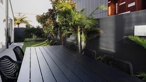 A modern outdoor patio with a dark wooden table and chairs, surrounded by lush greenery and a tall wall. - The Buller St Retreat (New Plymouth)